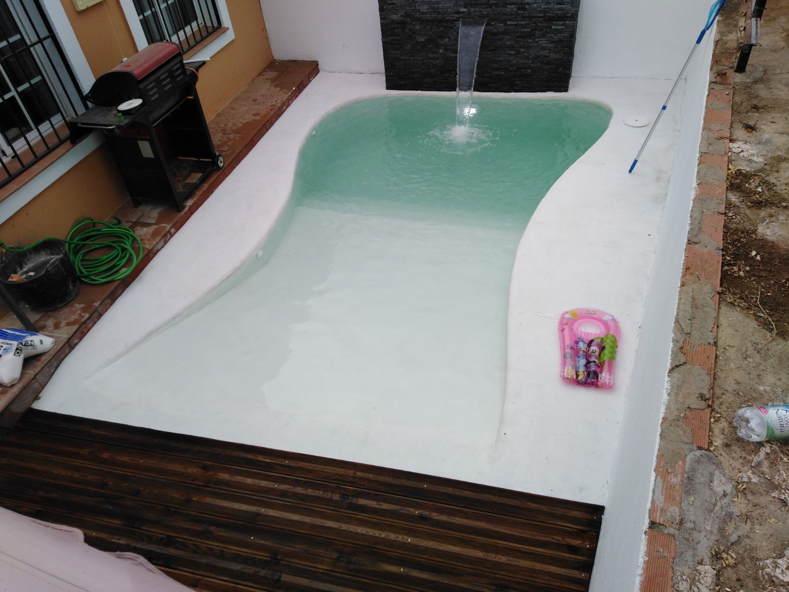 Ejemplo de piscina de formas suaves en un espacio pequeño, con cascada y entorno aún en obra.