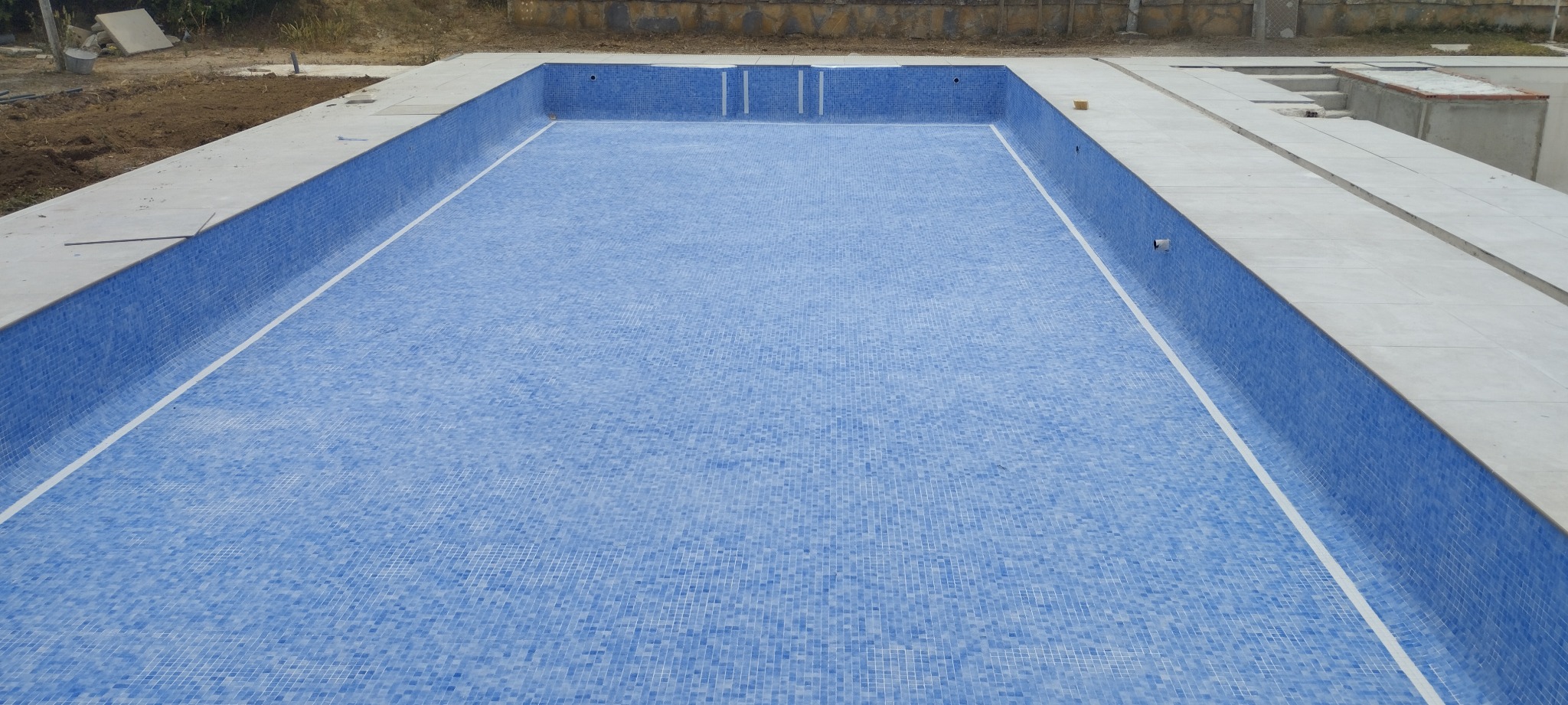 Piscina comunitaria de Manilva durante la reforma, con revestimiento de gresite y sin agua